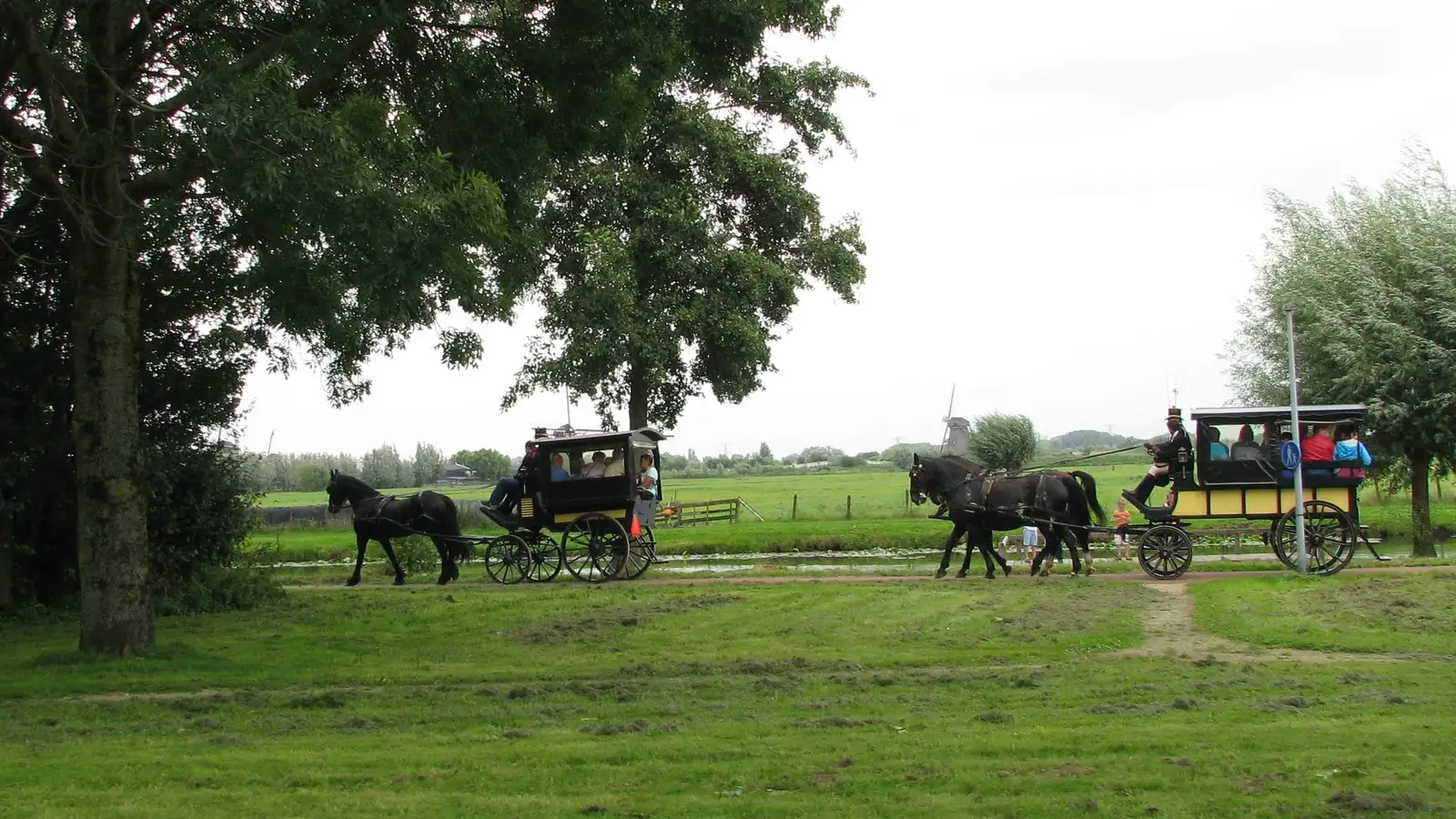 Twee janpleziers met zwarte paarden op een boerenpad met de molens van Kinderdijk
