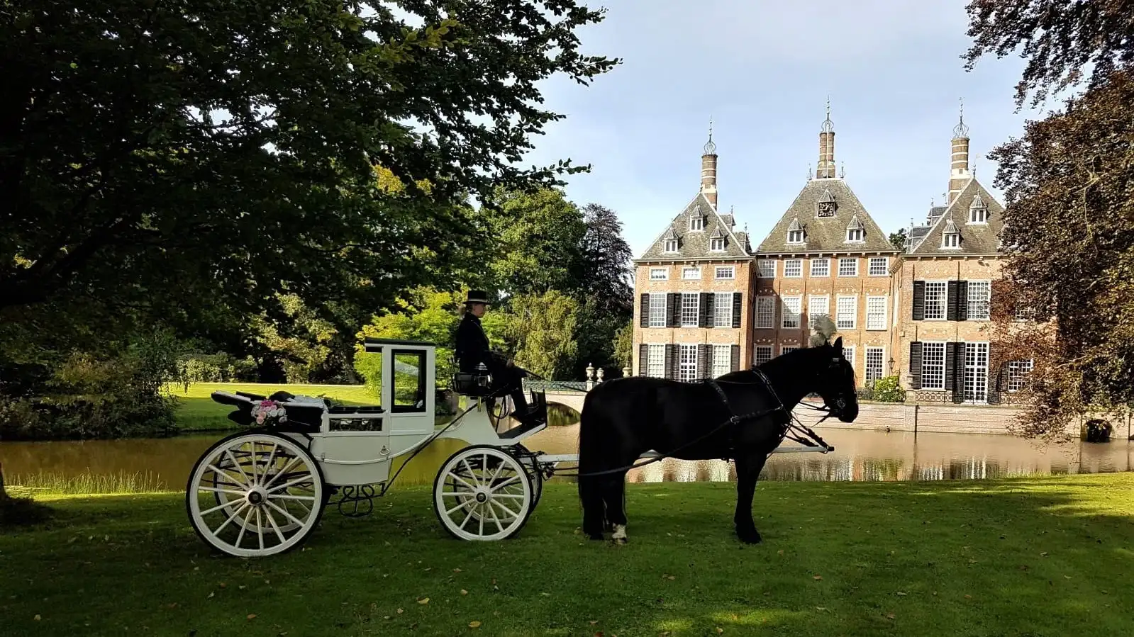Witte landaulet trouwkoets met zwart paard voor een kasteel met slotgracht