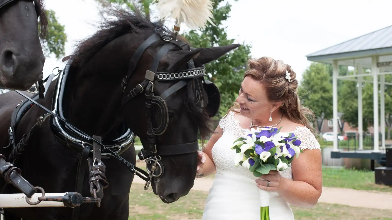 Bruid met bruidsboeket naast een zwart paard met witte pluim