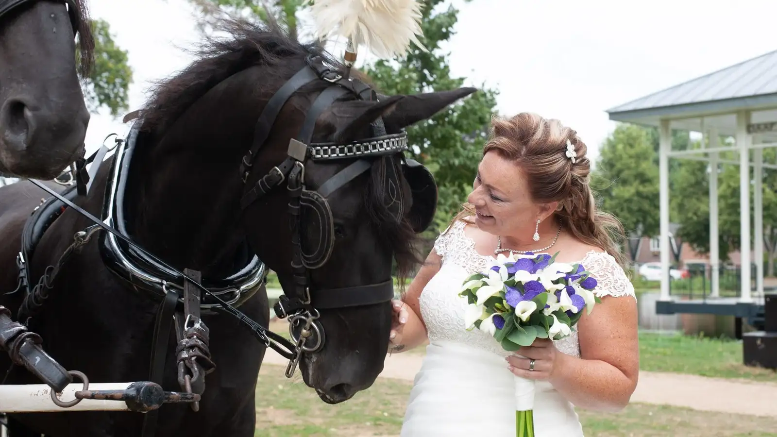 Bruid met bruidsboeket naast een zwart paard met witte pluim