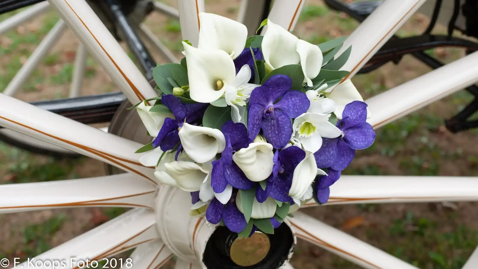 Detail van een wit koetswiel met een bruidsbloemstuk