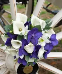 Boeket witte callalelies en paarse orchideeen op het wiel van de trouwkoets